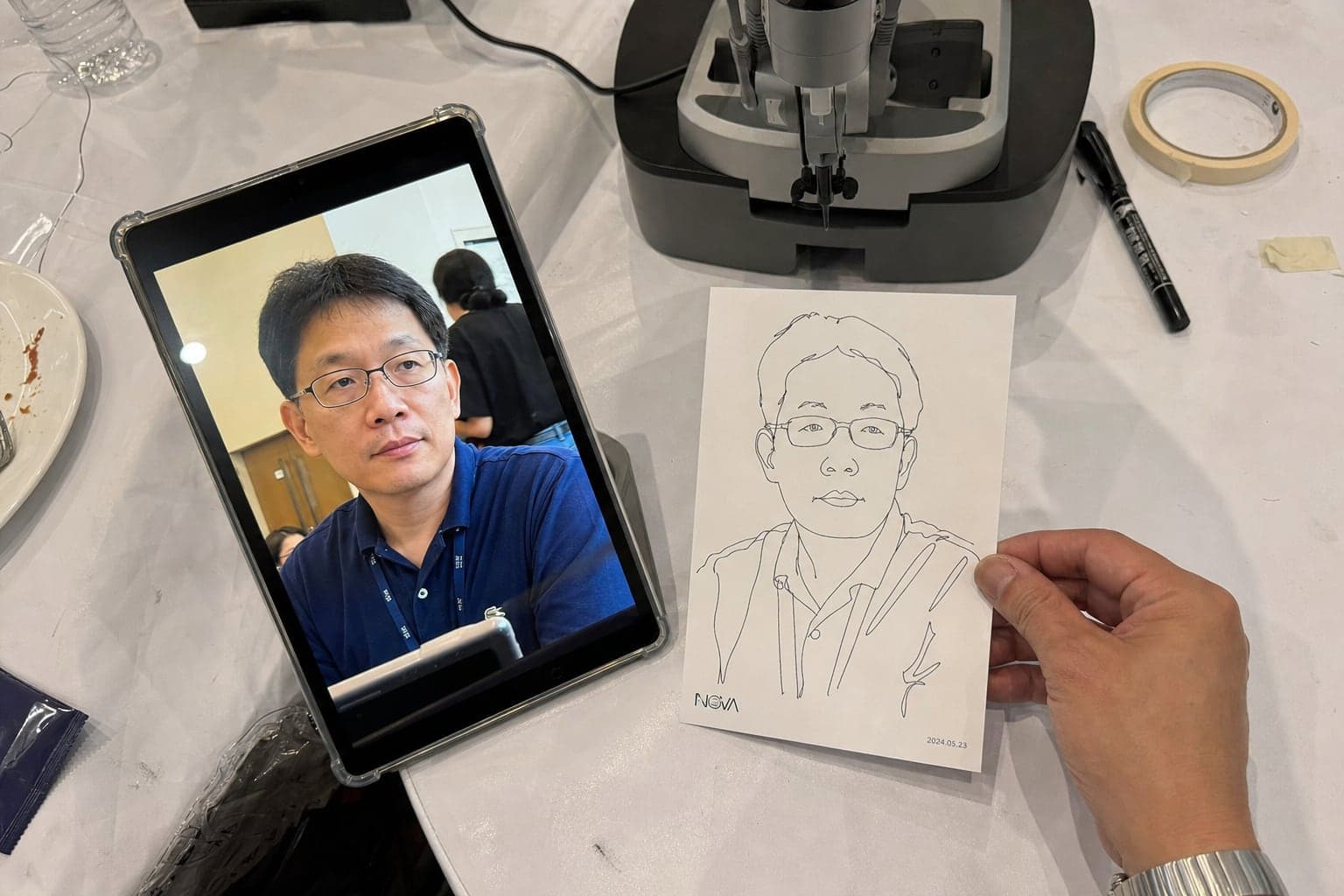 平板上的賓客原照與 AI 素描機器人畫完的 4×6 線稿並排